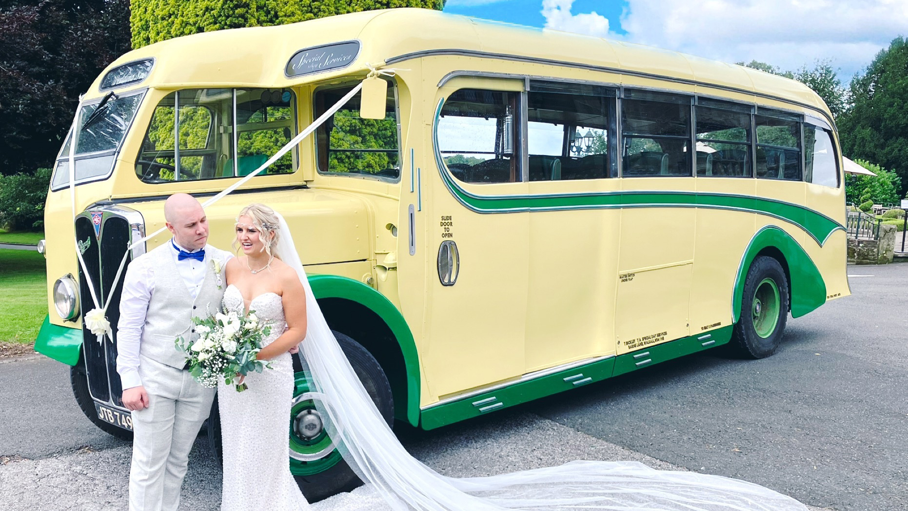 Yellow and green vintage single-decker bus shown from a side angled view with a bride and groom standing beside it in a car park area.