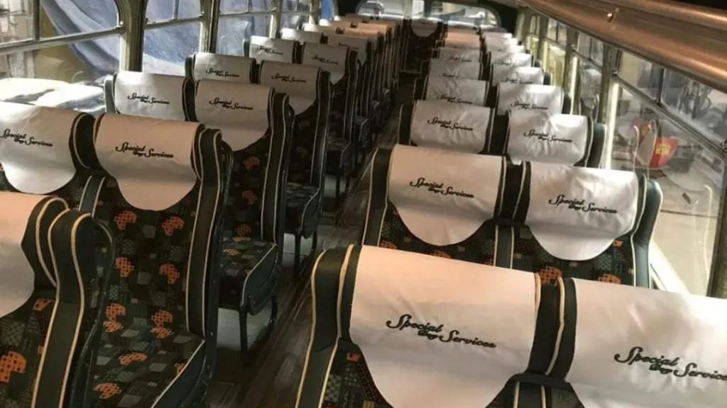 Interior of a vintage single-decker bus with patterned seats and white personalised fabric headrests, shown from the aisle looking forward.