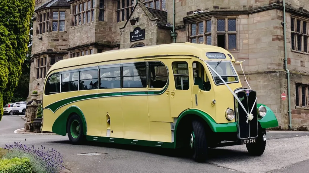 Yellow and green vintage single-decker bus photographed from a front angled view outside a large historic stone building