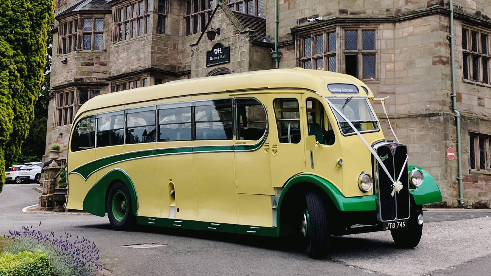 Yellow and green vintage single-decker bus photographed from a front angled view outside a large historic stone building