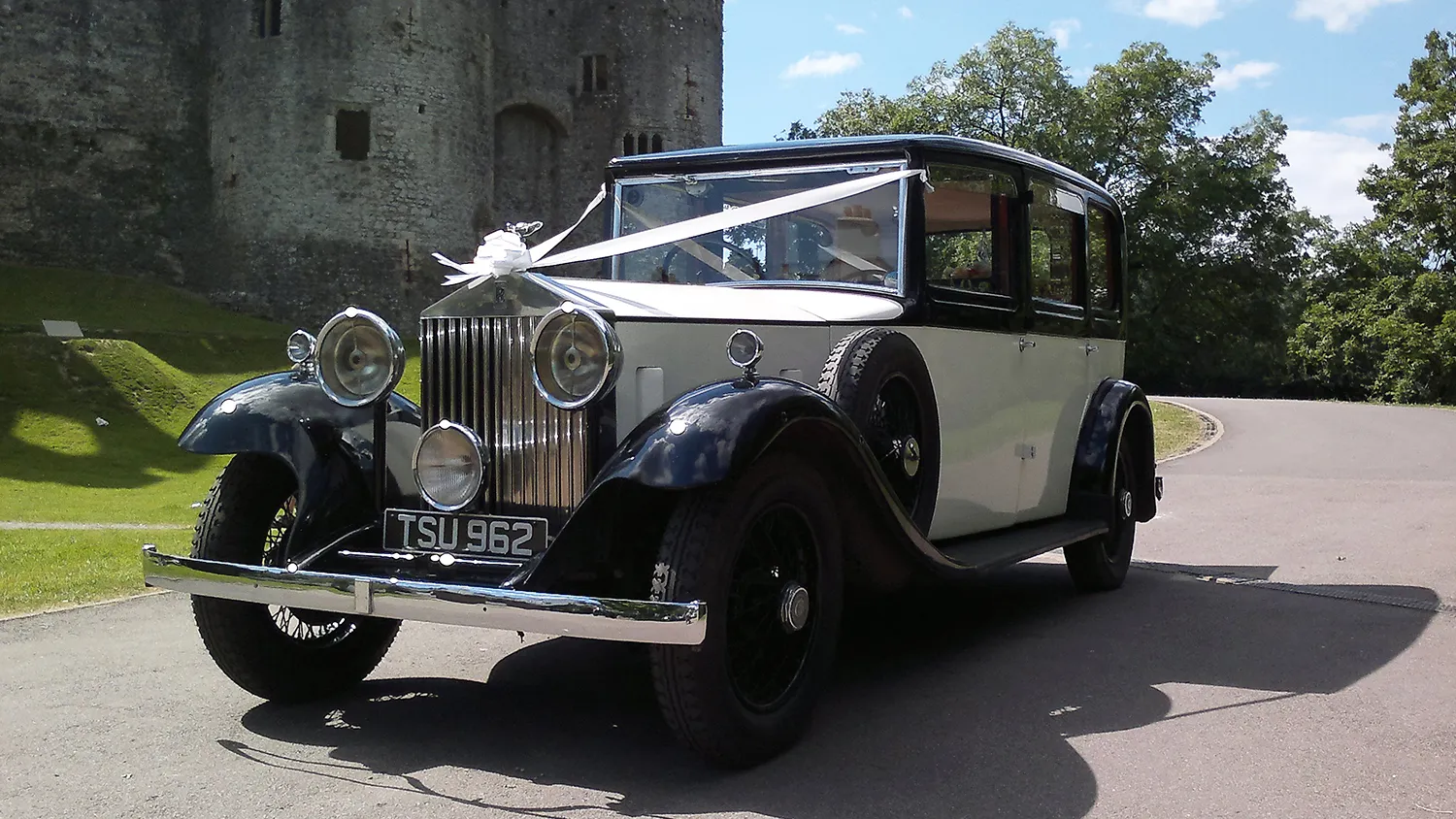 Vintage 1933 Rolls Royce 20/25 in black and white parked outside a stone building, showing its long bonnet, classic grille and elegant wedding-car styling.