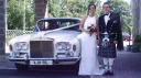 Bride and groom posing beside a 1974 white Rolls Royce Silver Shadow, showing its classic chrome grille and elegant 1970s styling.