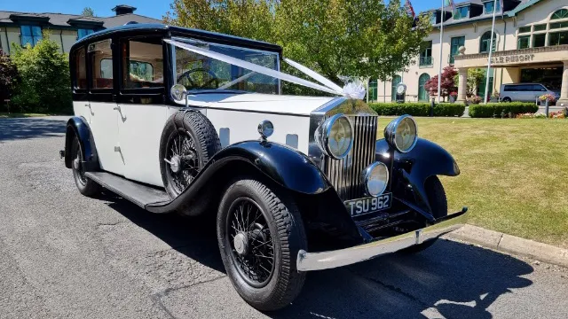 Black and white vintage Rolls Royce 20/25 Limousine parked on a driveway with sunny blue skies, highlighting the chrome headlights and extended rear cabin.