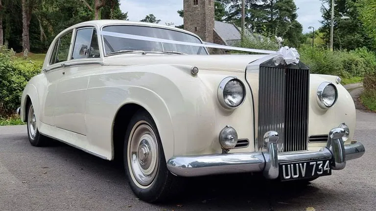 Front view of a classic Rolls Royce Silver Cloud Mk I in ivory, parked on a quiet road in Wales, showing its iconic grille, rounded wings and elegant 1950s styling.