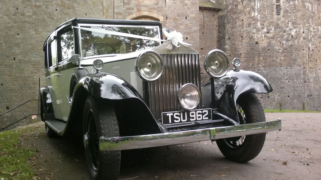 Front-facing view of a vintage Rolls Royce limousine decorated with white wedding ribbons, showing the imposing grille and polished chrome details.