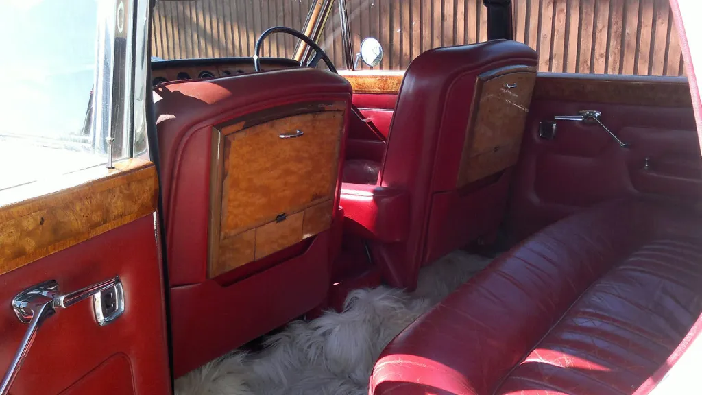 Rear seat area of the Rolls Royce Silver Shadow Mk I with red leather upholstery, wood veneer picnic tables and spacious classic 1960s interior styling.