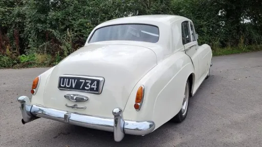 Rear view of the Rolls Royce Silver Cloud Mk I in ivory, displaying the smooth curved boot line, chrome bumper and vintage number plate.
