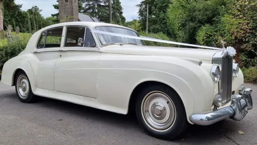 Side view of a Rolls Royce Silver Cloud Mk I wedding car in ivory, highlighting its long body shape, white-wall tyres and timeless 1950s luxury design.