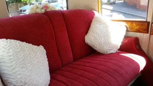 Close-up of the vintage Rolls Royce interior showing plush red velour seating with white cushions and classic wooden window surrounds.