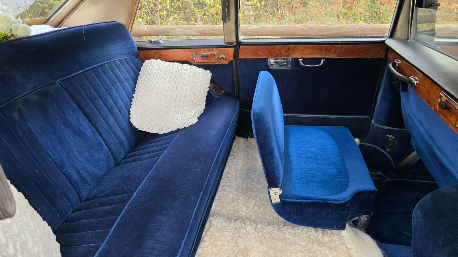 Blue velour interior of a classic Daimler limousine showing rear seating, wooden trim and white cushions.