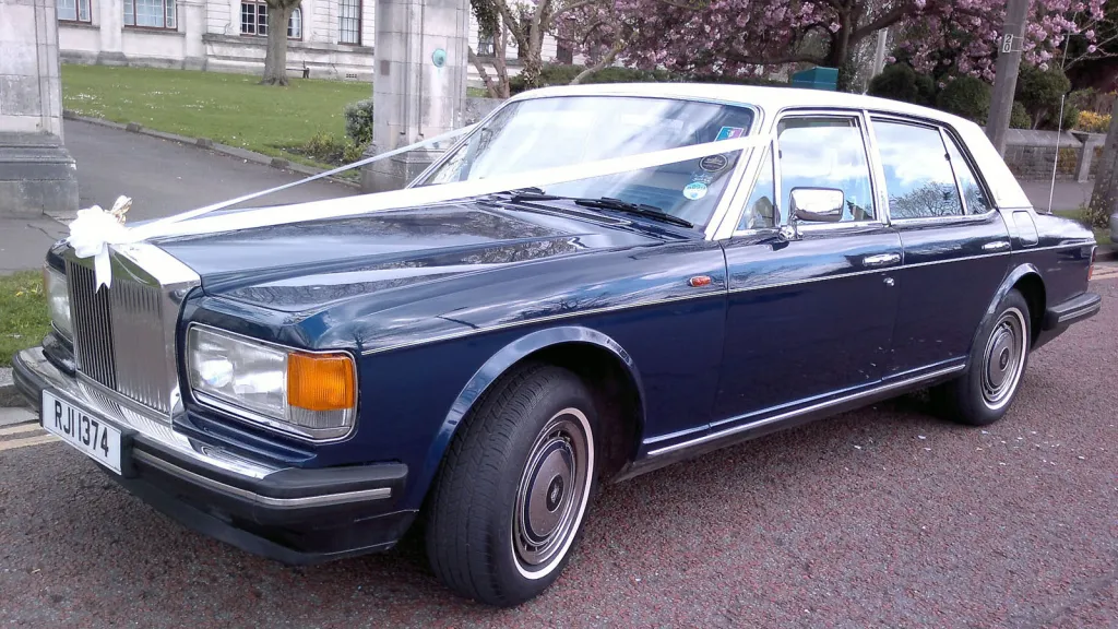 Front three-quarter view of a blue Rolls-Royce Silver Spirit with a white roof, parked on a residential street.