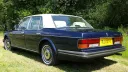 Rear view of a blue Rolls-Royce Silver Spirit with a white roof, showing chrome bumper and registration plate.