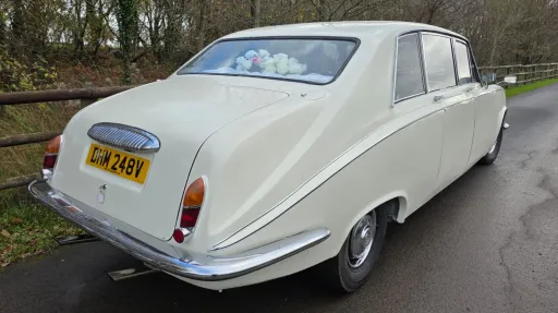 Rear view of a cream classic Daimler limousine parked on a rural road in Wales, showing chrome bumper and registration plate.