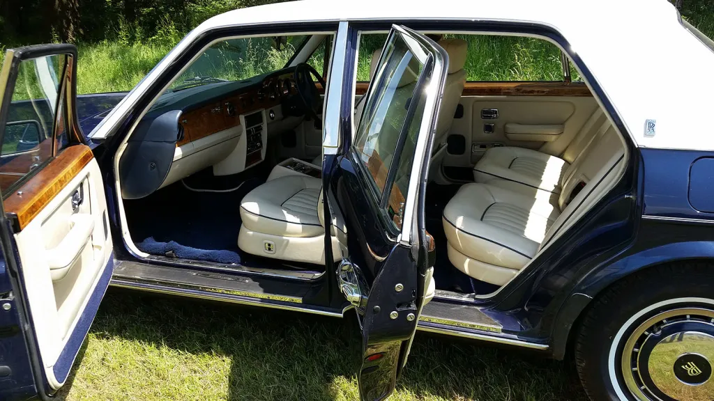 Side view of a blue Rolls-Royce Silver Spirit with white roof and both rear doors open, showing cream leather interior.