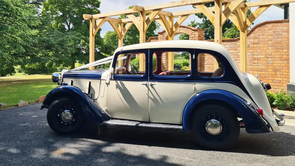 Blue and ivory 1937 Austin 10 Cambridge parked outdoors with sunroof open, showing its elegant two-tone paint and classic 1930s design, ideal for wedding hire in Leicester and Rutland.