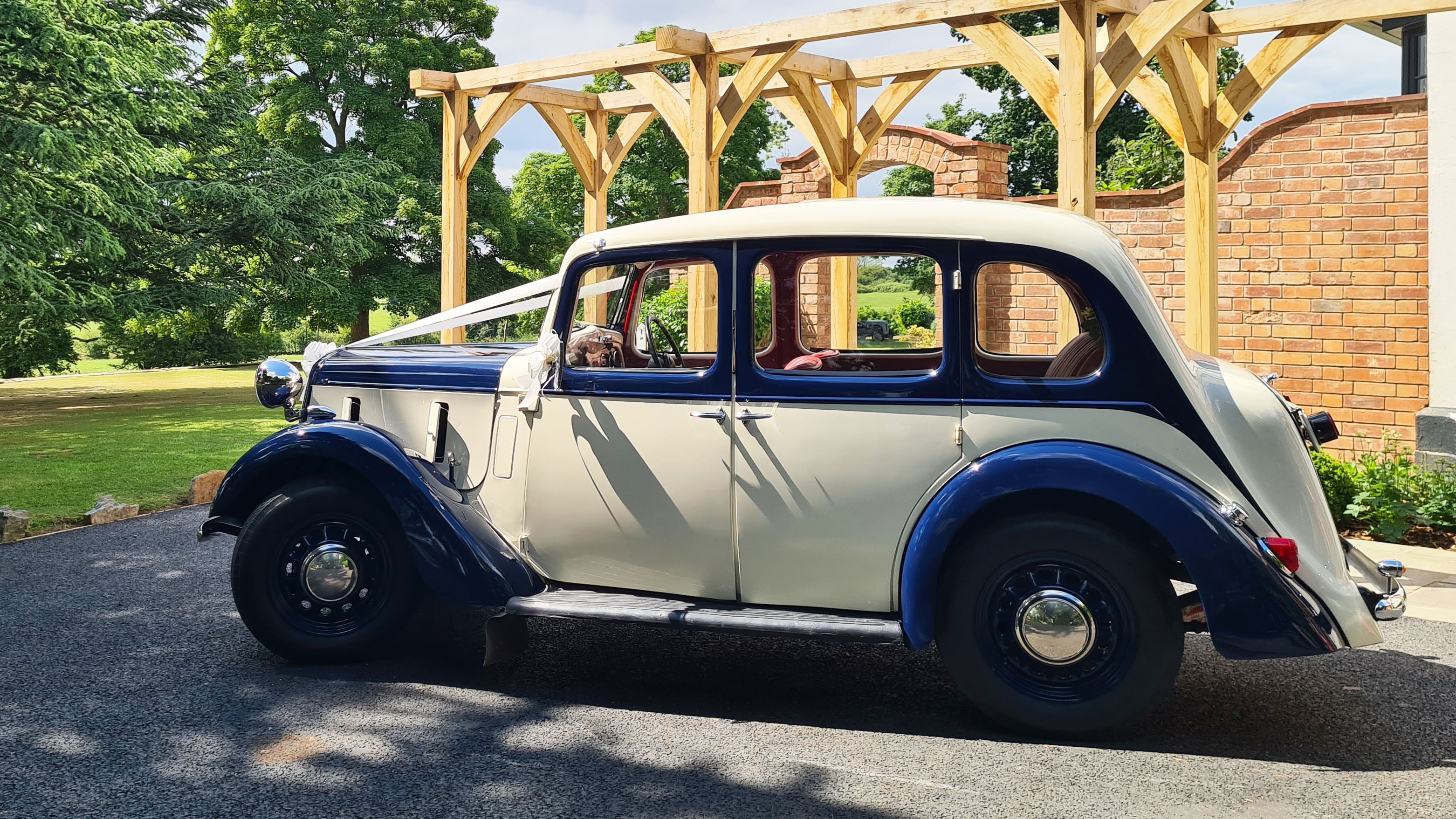 Blue and ivory 1937 Austin 10 Cambridge parked outdoors with sunroof open, showing its elegant two-tone paint and classic 1930s design, ideal for wedding hire in Leicester and Rutland.
