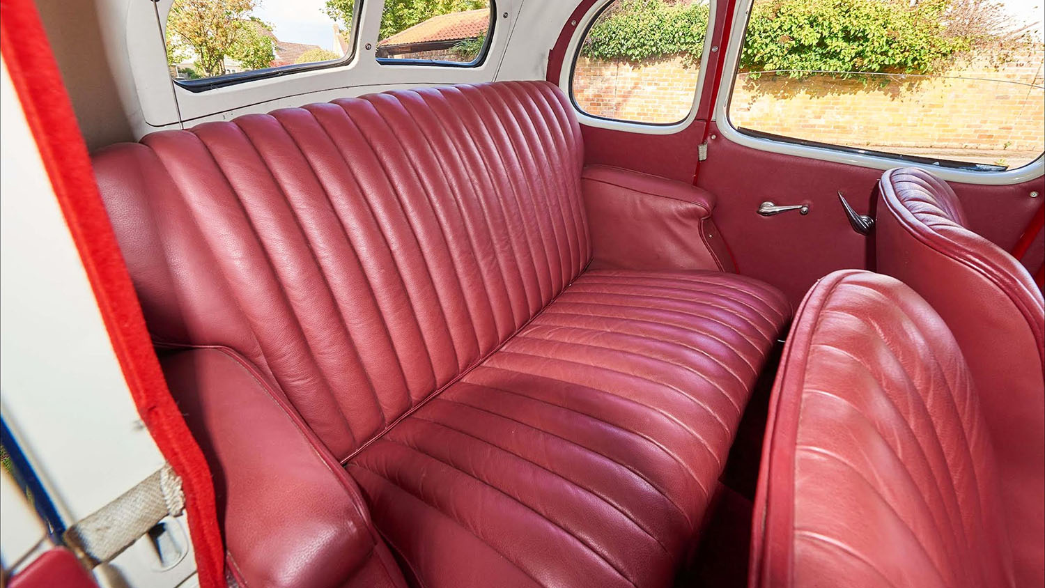 Close-up of the burgundy leather rear seats inside a 1937 Austin 10 Cambridge, showcasing its restored vintage upholstery and spacious period interior.