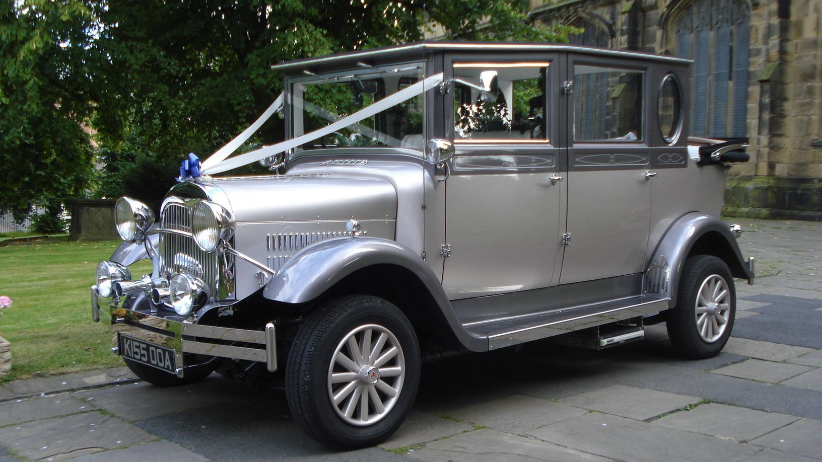 Silver imperial wedding car dressed with white ribbons and a blue bow