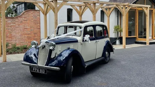 Three-quarter angle of the 1937 Austin 10 Cambridge showing the front grille and sweeping wings, photographed under a wooden pergola for Leicester wedding hire.