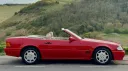 Side view of red Mercedes-Benz SL R129 convertible with roof down in countryside setting
