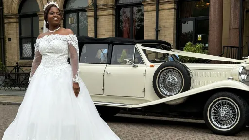 Bride standing beside an Old English White Beauford 4-door convertible wedding car outside a grand stone wedding venue