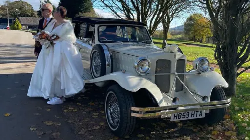 Bride and groom with an Old English White Beauford 4-door convertible wedding car during autumn wedding photographs