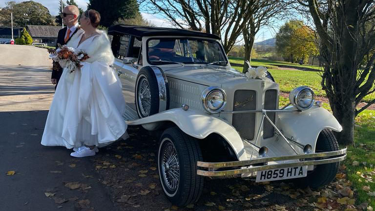 Bride and groom with an Old English White Beauford 4-door convertible wedding car during autumn wedding photographs