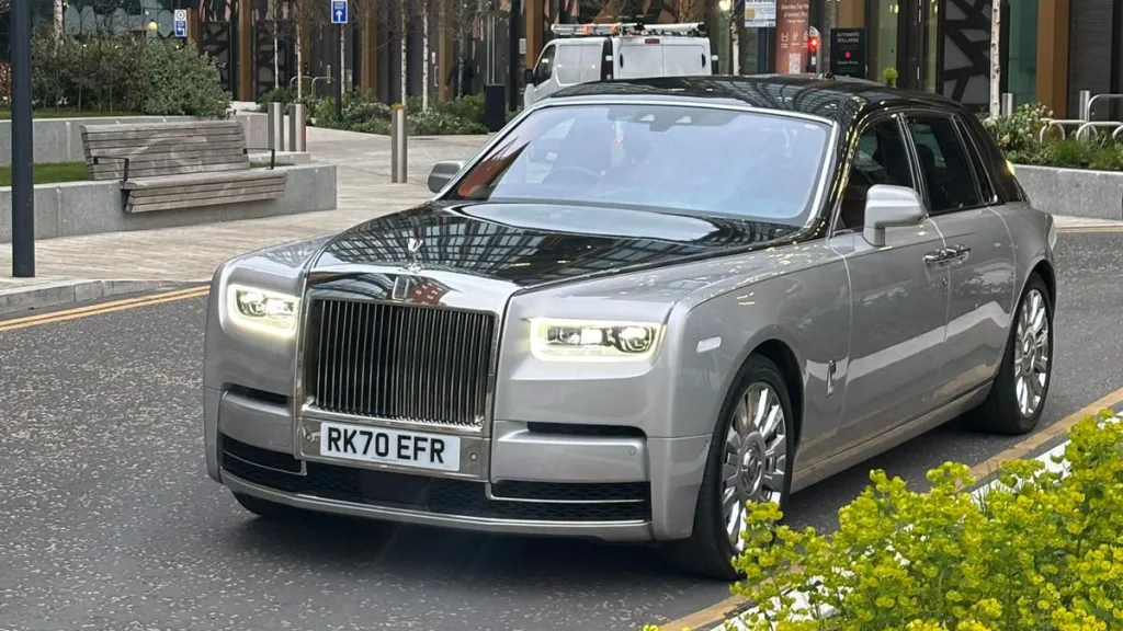 Black and silver Rolls-Royce Phantom VIII at dusk with headlights illuminated
