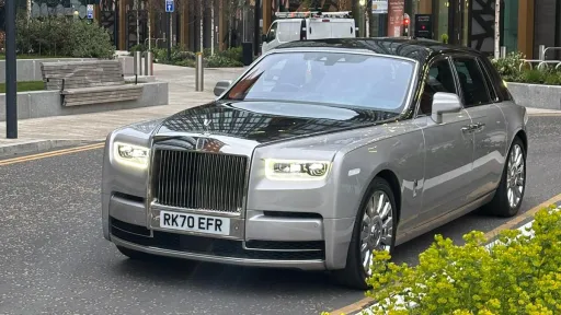 Black and silver Rolls-Royce Phantom VIII at dusk with headlights illuminated