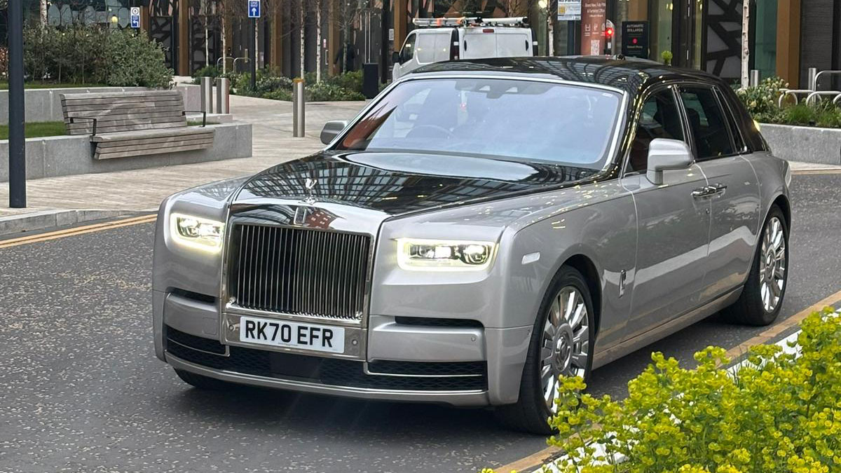 Black and silver Rolls-Royce Phantom VIII at dusk with headlights illuminated