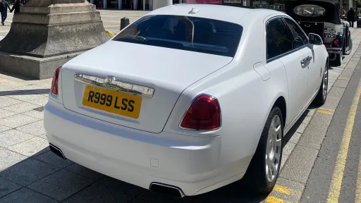 Rear view of a white Rolls-Royce Ghost wedding car parked on a city street, highlighting its elegant saloon styling