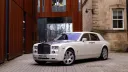 Front left side view of a white Rolls-Royce Phantom wedding car parked on a cobbled driveway outside a historic building