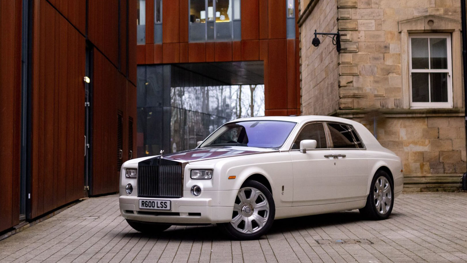 Front left side view of a white Rolls-Royce Phantom wedding car parked on a cobbled driveway outside a historic building