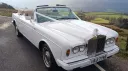 Front view of a white Rolls-Royce Corniche convertible wedding car with roof down, set against a countryside backdrop