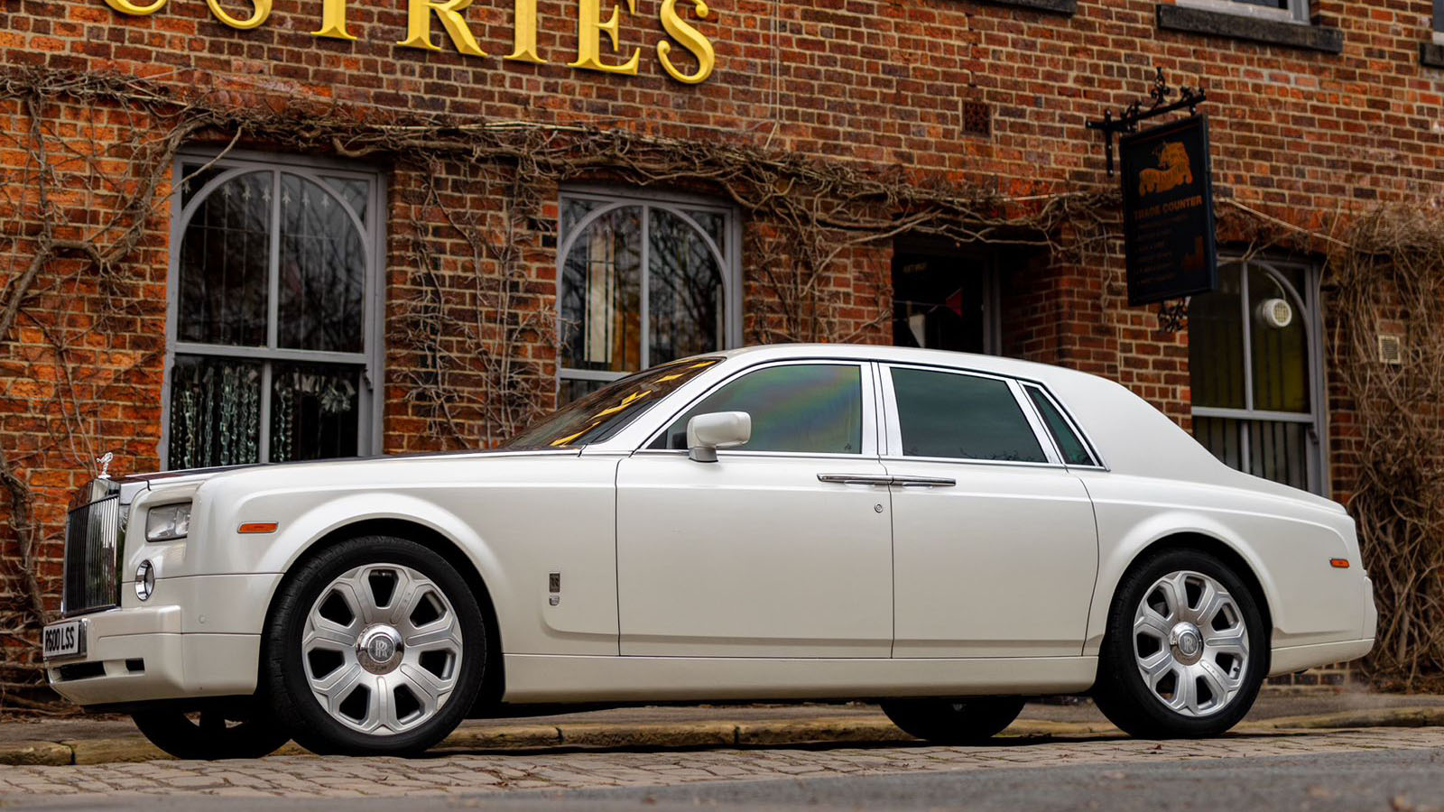 Left side profile of a white Rolls-Royce Phantom wedding car highlighting its long wheelbase and elegant limousine styling