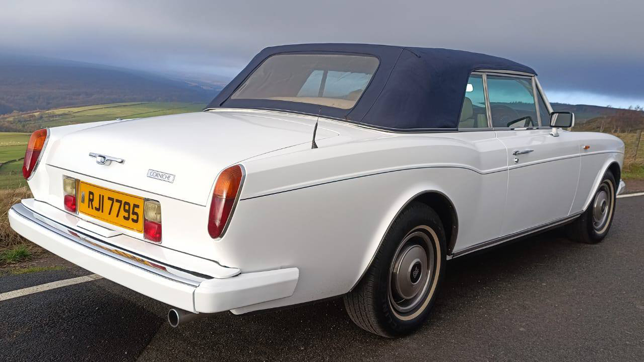 Rear view of a white Rolls-Royce Corniche wedding car with blue soft top raised, photographed on a scenic country road