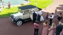 Aerial view of a cream 1930s style Imperial vintage wedding car surrounded by wedding guests outside the ceremony venue.
