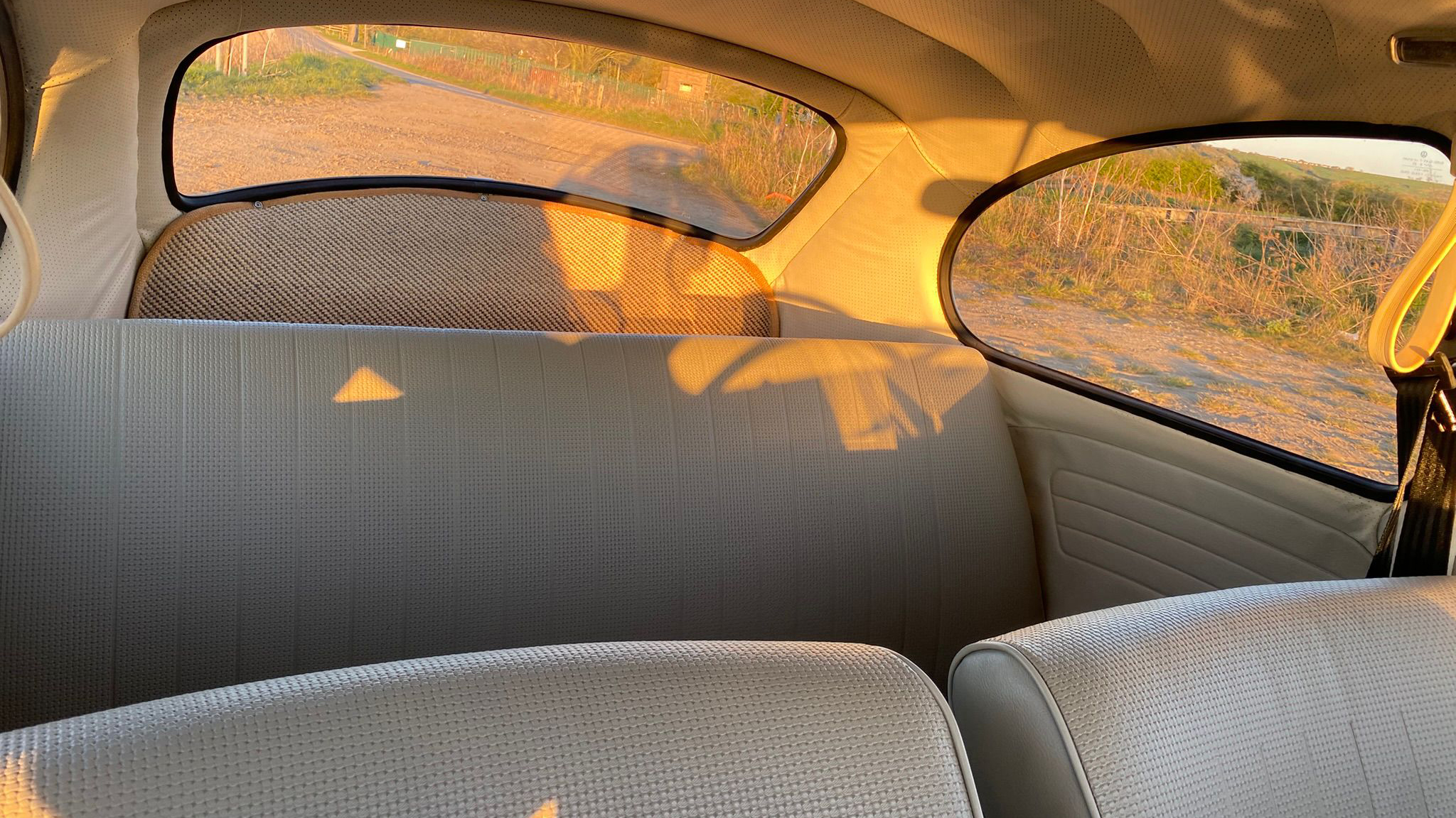 Cream interior of a classic Volkswagen Beetle showing rear seating, curved rear window and warm vintage upholstery