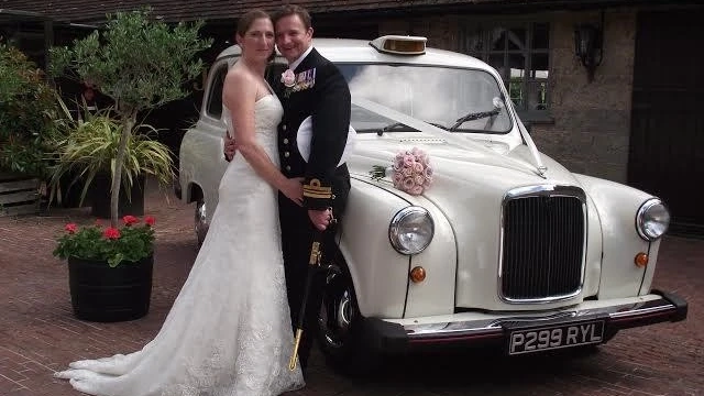 Bride and groom posing beside a classic London wedding taxi finished in cream with traditional grille and chrome details.