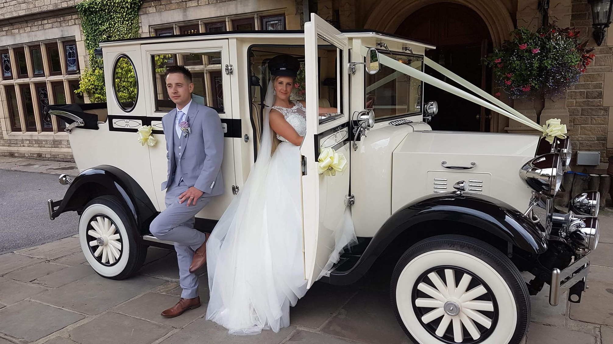 Bride and groom posing next to a cream vintage Imperial wedding car in classic 1930s styling.