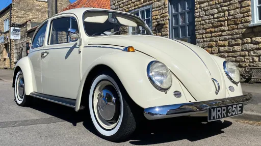 Cream classic Volkswagen Beetle parked outdoors, ideal for wedding car hire with chrome detailing and whitewall tyres
