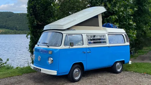 Blue Bay Window Volkswagen Campervan Westfalia parked by a lakeside with pop-top roof raised.