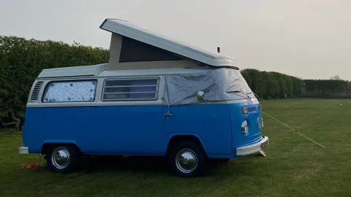 Blue Bay Window VW Campervan Westfalia prepared for wedding hire with pop-top roof raised in a countryside setting.