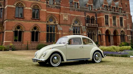 Cream Volkswagen Beetle wedding car parked on lawn outside a historic red brick wedding venue