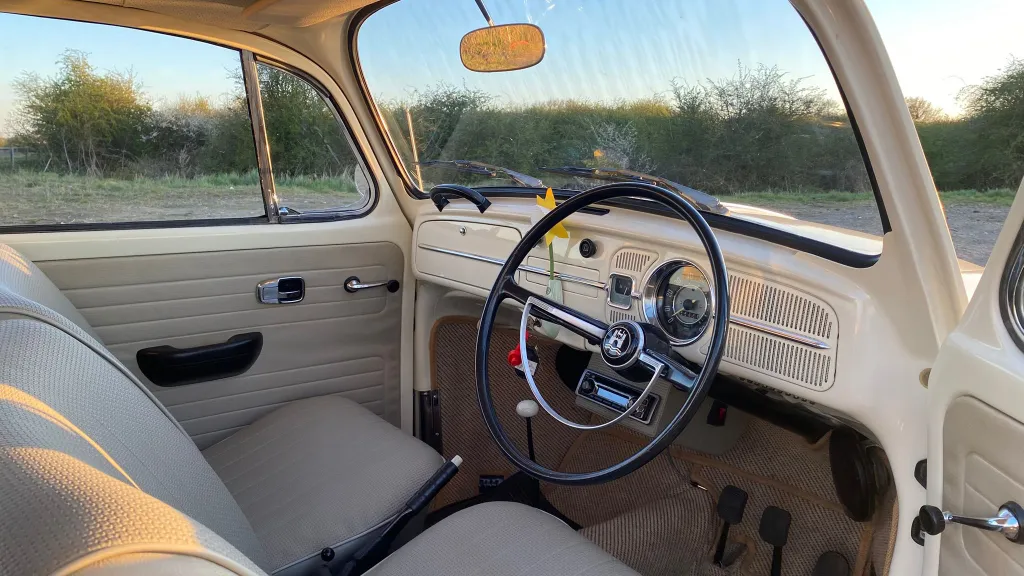 Front interior of a classic Volkswagen Beetle featuring original steering wheel, dashboard and cream trim