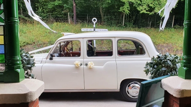 Side view of a cream classic London taxi wedding car showing its spacious rear cabin and traditional shape.