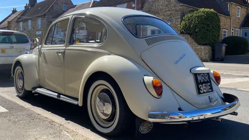 Rear left view of a cream classic Volkswagen Beetle showing iconic curved rear window and chrome rear bumper