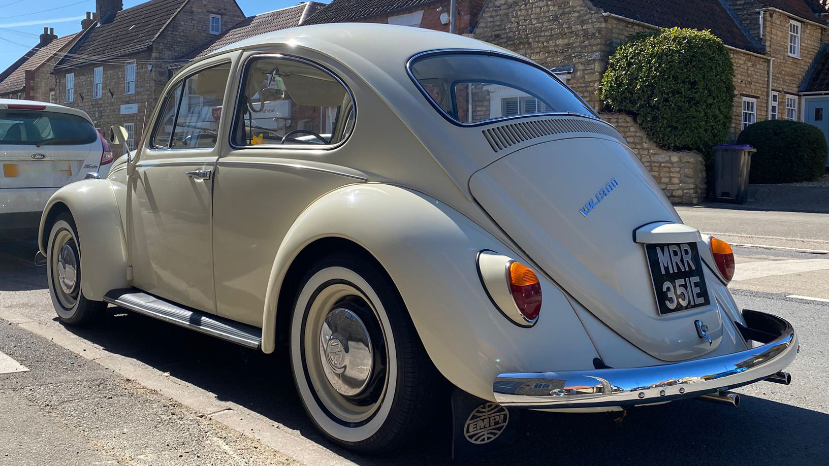 Rear left view of a cream classic Volkswagen Beetle showing iconic curved rear window and chrome rear bumper