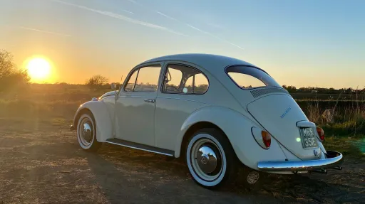 Rear left view of a cream classic Volkswagen Beetle at sunset, highlighting its timeless shape and wedding appeal