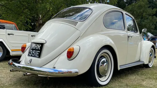 Rear right view of a cream classic Volkswagen Beetle wedding car with chrome detailing and whitewall tyres